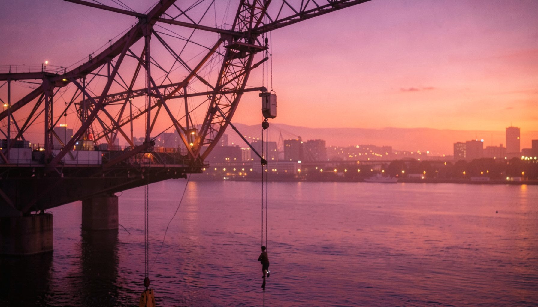 Pont suspendu aux tours rouges enjambant une étendue d'eau au crépuscule, lumières urbaines en arrière-plan, ambiance calme